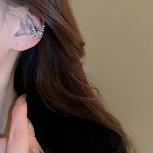 Detail of silver metallic butterfly ear cuff with a hollow 3D design on model's ear