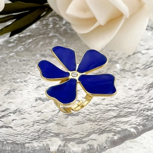Gold open ring with blue oil-drop flower and crystal center on a glass surface