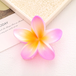 Detail of a pink and yellow gradient plumeria flower shark hair claw clip in a flat lay