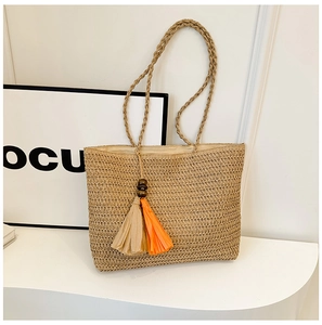 Close-up of khaki straw beach tote featuring vibrant orange and beige tassel charms