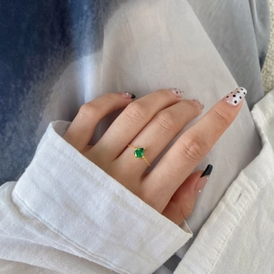 Close-up of golden chain ring with teardrop emerald gemstone on a female model