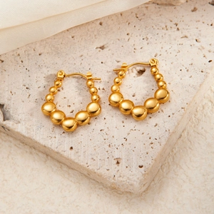 Detail of gold beaded hoop earrings featuring gradient sphere design on a stone surface