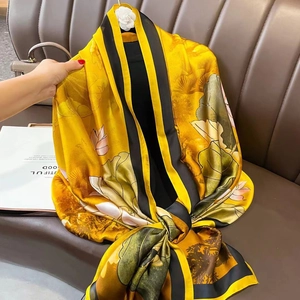 Elegant yellow silk-like scarf with lotus pattern and black border on a leather sofa