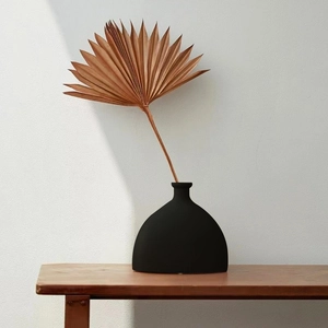 Minimalistische mattschwarze Keramikvase im halbkreisförmigen Design auf Holztisch