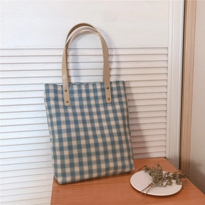 Detail of vintage blue plaid canvas tote bag featuring premium leather handles and rivets
