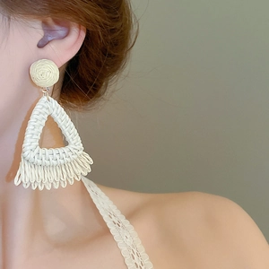 Vue détaillée des boucles d'oreilles bohèmes en raphia tressé avec pompons sur mannequin