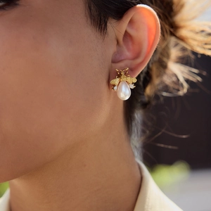 Detail showing bee-shaped gold earrings with teardrop pearl pendants worn on a model
