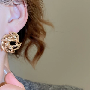 Detail of a model wearing a gold twisted knot earring with a polished metallic finish