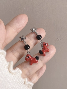 Detail of star-shaped earrings with black beads and red glazed rocking horse charms