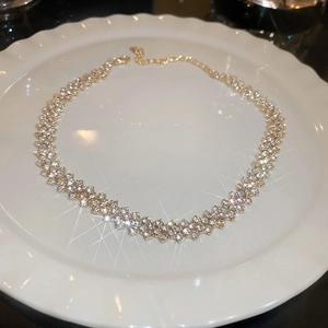 Close-up of golden rhinestone choker necklace on white ceramic tray with starburst lighting