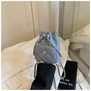 Close-up of blue denim mini bucket bag with gold camellia ornament and chain strap