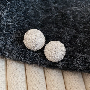 Close-up of minimalist silver round stud earrings with sparkling frosted sand texture