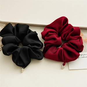 Detailed view of glossy satin scrunchies in black and burgundy with gold charms