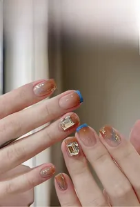 Detail of luxury press-on nails with blue tips, gold foil, and large rectangle rhinestones