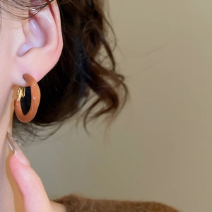 Detail of a minimalist caramel resin round hoop earring worn on a model's ear