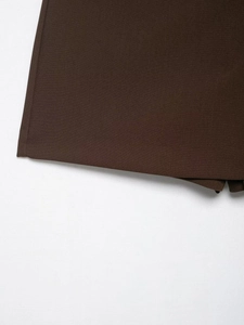 Close-up of asymmetrical hem on dark brown plain weave trousers with sharp needle stitching