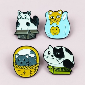 Detail showing four colorful enamel cat pins with artistic box designs in pink background