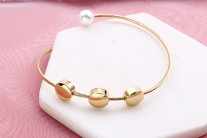 Detail of gold open bangle with wire texture, white pearl and metal discs on base