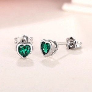 Macro view of dainty silver heart studs featuring emerald green zircon heart stones