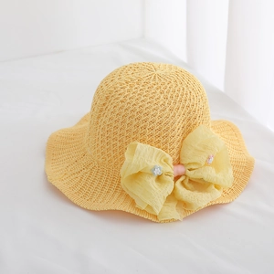 Detail of yellow straw hat featuring a translucent tulle bow and handmade floral accents