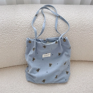 Close-up of blue corduroy tote bag featuring brown bear patterns and metal snap button