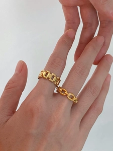 Detailed close-up of chunky gold-colored chain rings and link band rings on a hand