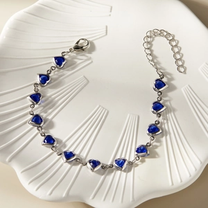 Macro detail of a silver bracelet featuring eleven heart-shaped blue glass stones on a white tray
