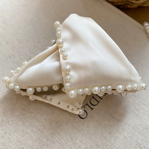 Détail de la pince à cheveux en satin crème avec bordure en perles et clous en métal