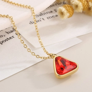 Detailed macro shot of a gold necklace with a vibrant red triangle crystal on a vintage paper