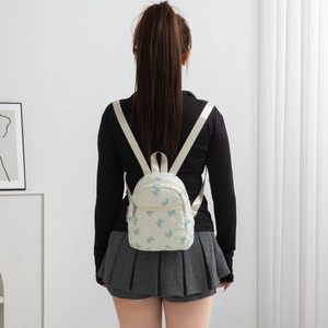 Close-up of a small cream quilted backpack featuring blue butterfly patterns on model