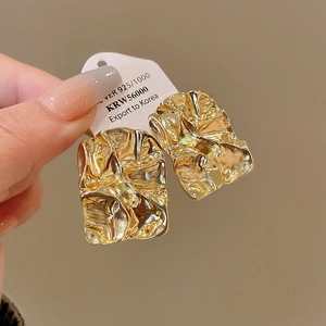 Close-up of gold geometric earrings featuring a unique hammered metal texture and 925 silver finish