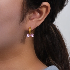 Close-up of golden hoop earring with two purple heart-shaped zircons in butterfly design