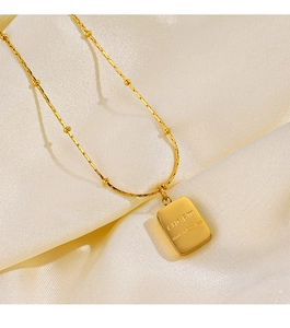 Detailed view of 18K gold plated rectangular pendant with CHARM engraving on silk fabric