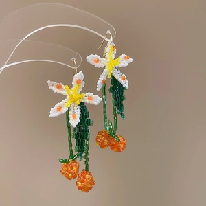 Detail of handmade beaded flower earrings with orange berry tassels and green leaves