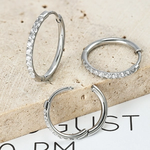 Set of three silver stainless steel hoop earrings with white zircon on stone background