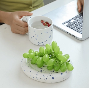 Polka dot ceramic mug with oversized handle and matching saucer on white desk