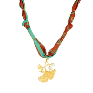 Detail of ginkgo leaf gold pendant with three white pearls on red and green silk ribbon