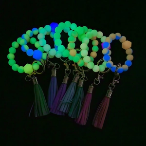 Luminous silicone bead keychain bracelet with tassel glowing in dark on black background