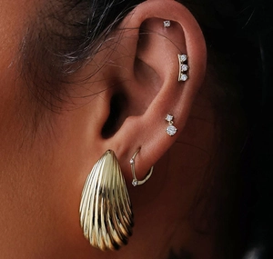 Macro shot of gold shell textured earring and sparkling zircon stud set on ear