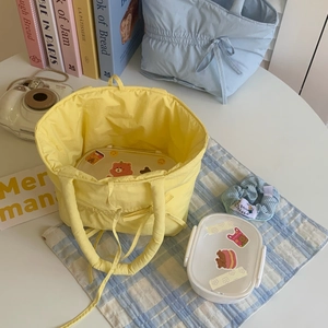 Detail of yellow pleated fabric bag with white lunch box on a picnic table setup