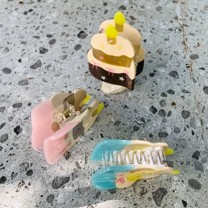 Detailed view of three acetate cake-shaped hair claws with candle and bow accents