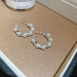 Macro view of C-shaped silver hoop earrings with white pearls and zircon pavé detail