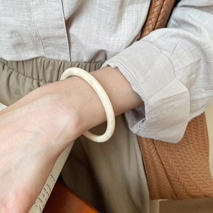 Detail view of cream resin bangle with marble texture worn by a model in French style