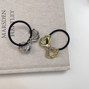 Close-up of gold and silver metal bow hair ties on a minimalist gray book background