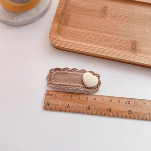 Detailed view of a 6.5cm milk tea knit hair clip with lace edges and cream heart