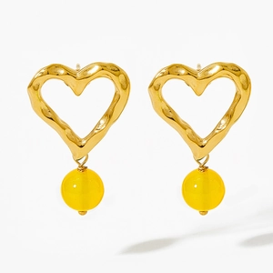 Close-up of golden wavy heart earrings with bright yellow resin beads on white background