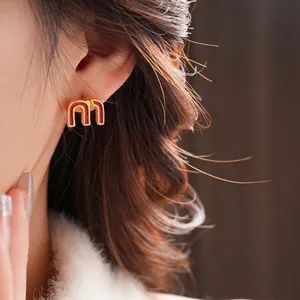 Golden M-shaped letter stud earrings with red enamel on female model for daily wear