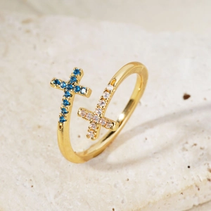 Close-up of gold cross ring featuring blue and white zircon stones on stone surface