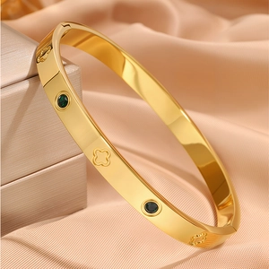 Detail of gold titanium steel bangle with clover engravings and green gemstone inlays