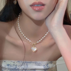 Detailansicht einer eleganten Perlenkette mit goldenem Herzanhänger und kleinen Kristallen